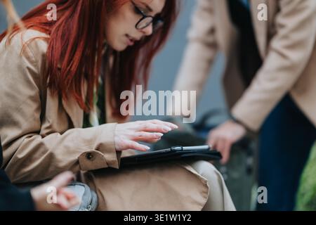 Business workers collaborating outdoors as a red-haired woman uses a tablet while colleagues stand nearby Stock Photo