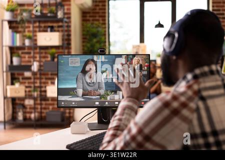 Professional african american man sitting at desk, actively speaking during video call. Remote team leader in virtual meeting, collaborating with shareholders on marketing and business strategy. Stock Photo