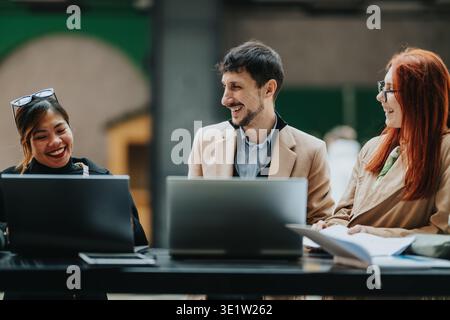 Business workers collaborating and laughing outdoors with laptops during a casual team meeting Stock Photo