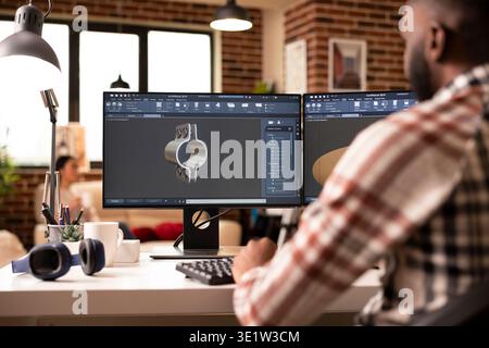 Creative male developer using cad software in brick wall apartment, designing 3d models for construction. African american man seated at workstation creating industrial tool prototypes in home studio. Stock Photo
