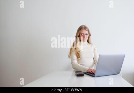 Smiling woman working on laptop at home. Online work, remote job and digital lifestyle concept with copy space. Stock Photo