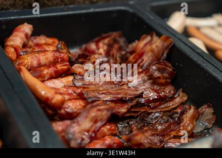 Trays of bacon strips and bacon wrapped sausages in buffet setup Stock Photo