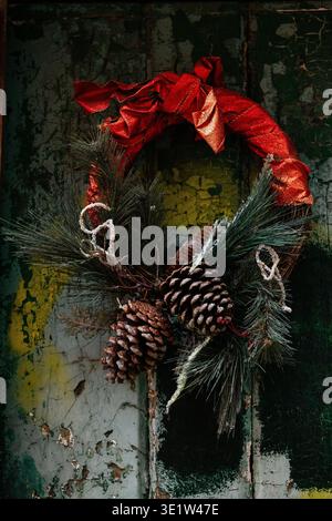 A red ribbon adorns a Christmas wreath made from pine cones and needles on an old, peeling, painted doorway. Stock Photo