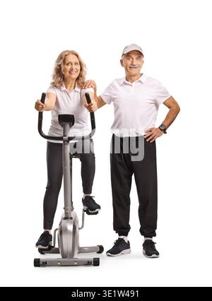Mature woman sitting on an exercise bike and senior man standing next to her isolated on white background Stock Photo