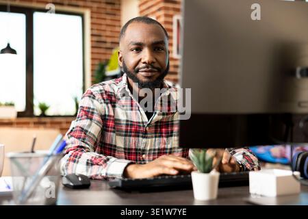 Focused african american entrepreneur works from home on desktop computer, reviewing marketing data and updating company financial reports before deadline. Serious, goal driven remote worker. Stock Photo