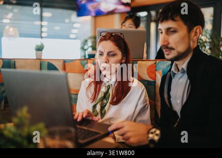 Business workers collaborating over laptop in a modern cafe discussing urgent project details Stock Photo