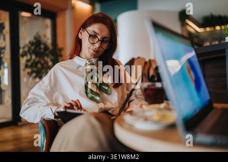 Businesswoman working on laptop and tablet in a relaxed cafe setting with coffee and notebook Stock Photo