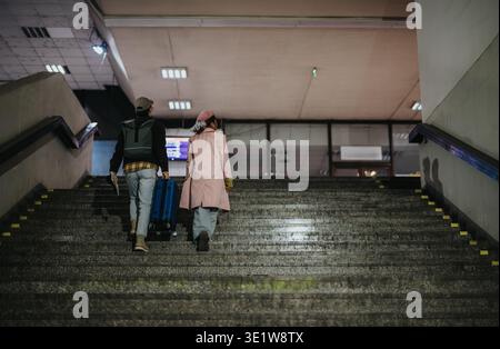 Young couple walking up train station stairs with blue suitcase while traveling together Stock Photo