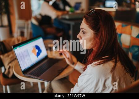 Business worker woman reviewing charts on laptop in a casual cafe coworking space Stock Photo