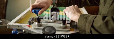 Header of Young Adult Man Operating Screen Printing Machine in Workshop Stock Photo