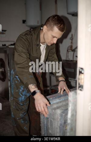Vertical of Young Adult Man Working with Silkscreens in Industrial Workshop Stock Photo