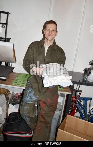 Vertical of Young Adult Man Holding Folded Shirts in Industrial Workspace  Stock Photo