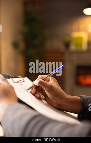 Professional therapist taking notes during counseling session, evaluating mental health assessment of client. African American psychologist writing in notepad, providing supportive therapy services. Stock Photo