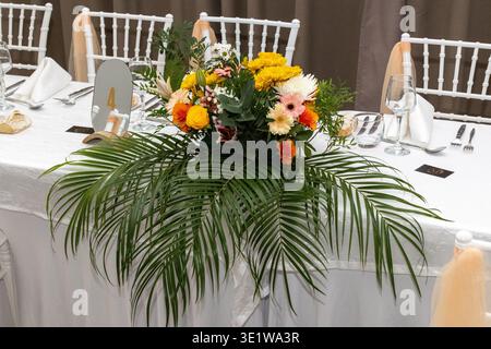 Elegant wedding reception table featuring a vibrant floral centerpiece with tropical leaves and colorful flowers. Stylish banquet setup with refined t Stock Photo