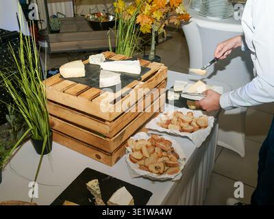 Caterer serving slices of cheese with bread from a rustic display on wooden crates. Buffet setup highlighting gourmet food presentation and hospitalit Stock Photo