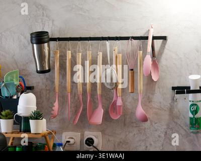 Collection of kitchen utensils hanging on a wall rack in a modern home kitchen. Organized cooking tools including spatulas, ladles, and whisks, ideal Stock Photo
