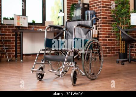 Closeup of wheelchair placed in middle of vacant workspace, with computer and business documents on desk in background. Shelves and plants complementing the spacious, organized brick wall office. Stock Photo