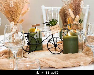 Close-up of a rustic wedding table centerpiece featuring candles, dried flowers, and a decorative miniature bicycle. Elegant and cozy table decoration Stock Photo