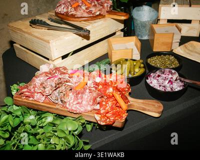 Rustic charcuterie setup with assorted cured meats displayed on wooden boards, accompanied by pickles, onions, and condiments. Gourmet appetizer Stock Photo