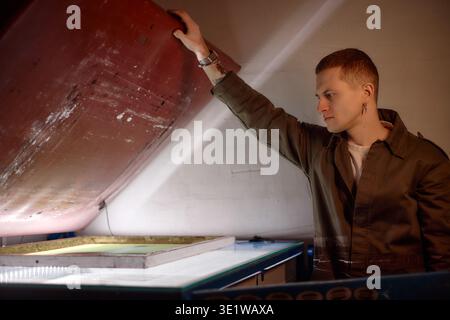 Young Man Operating Industrial Screen Printing Equipment Indoors Stock Photo