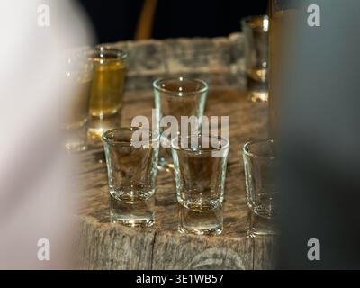 Close-up of small shot glasses arranged on a rustic wooden table, capturing a casual bar or party setting with alcohol drinks ready to be served. Stock Photo