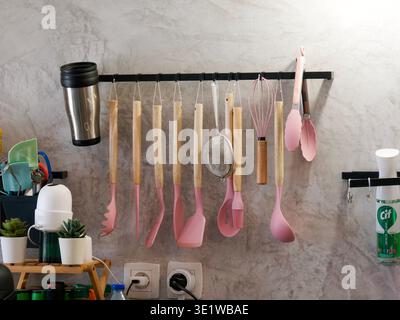 Kitchen utensils including spatulas, whisk and ladle neatly arranged on a wall-mounted rack, showcasing an organized and functional home kitchen setup. Stock Photo