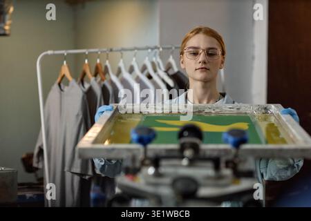 Young Woman Screen Printing T Shirt in Workshop Setting Stock Photo