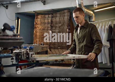 Young Man Operating Screen Printing Machine in Industrial Workshop Stock Photo