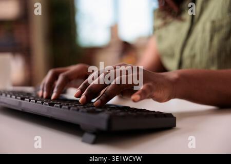 Closeup of african american influencer writing post for social media on computer keyboard while working remote from home living room. Selective focus on woman hands typing blog article. Stock Photo