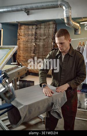 Vertical of Young Man Preparing Fabric on Screen Printing Machine in Workshop Stock Photo