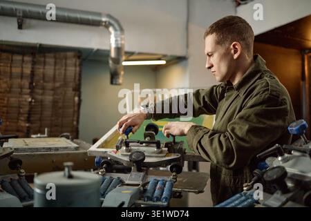 Young Adult Man Operating Industrial Printing Machine in Workshop Stock Photo
