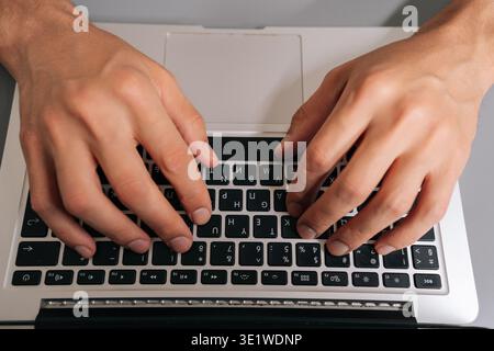 High-angle view of unrecognizable freelancer male typing on laptop keyboard, professional home office scene showing remote work, coding, online Stock Photo