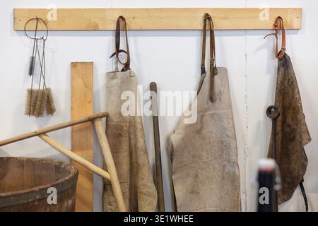 Several rustic aprons and wooden tools are hanging on a Brewery wall suggesting a crafting or workshop environment. The scene includes brushes buckets Stock Photo
