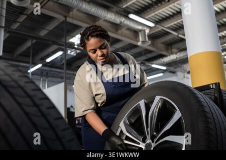 A dedicated female mechanic focuses on changing a tire in a lively garage setting. Stock Photo