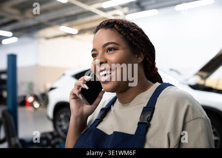 Smiling African American mechanic talks on her phone while working in the garage. Stock Photo