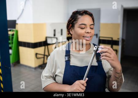 Confident African American woman in overalls works with tools at an auto repair shop. Stock Photo