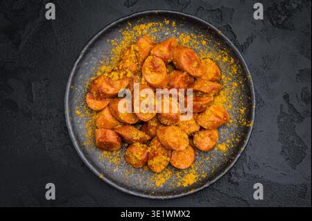 German currywurst, sausages with curry spice served on rustic metal plate over dark textured background perfect for street food and stock imagery Stock Photo