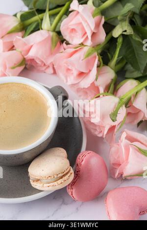 Vintage granite color coffee cup, pink rose flowers and french sweet cookies macarons macaroons on marble background. Heart shape macarons, cup and bo Stock Photo