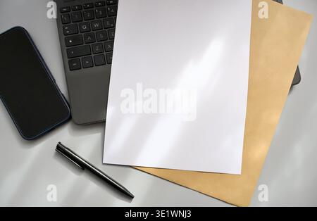 Flat lay of office workspace with laptop, smartphone, pen and blank white paper sheet for copy space or mockup. Stock Photo