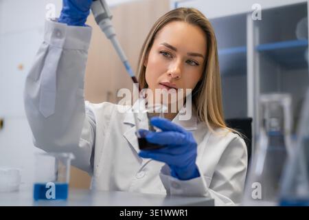 Conducting meticulous sample transfer using a pipette to add dark biological liquid into beaker at laboratory workstation. Stock Photo