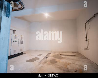 A large, empty room with a white wall and a grey floor. The room is empty and has no furniture Stock Photo