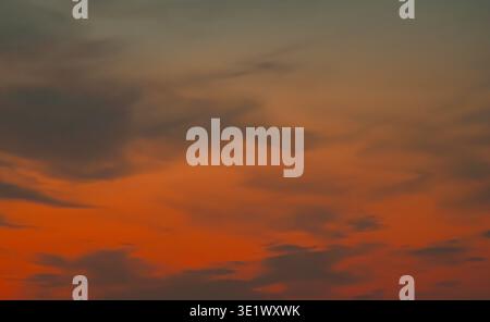 Atmospheric twilight view featuring heavy dark grey clouds and a narrow brilliant orange light streak along the natural evening horizon. Stock Photo