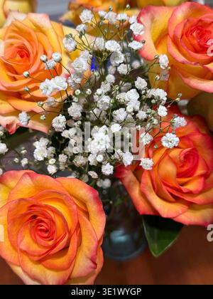 Looking down at a floral bouquet filled with yellow and coral Sunset Roses with Baby's Breath in a vase on a table with selective focus Stock Photo