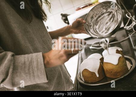 Créteil, France - April 27, 2019: A woman pours white sugar glaze over traditional Easter breads, preparing for the holiday feast in Créteil. Stock Photo