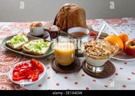 Rich breakfast on table, food arrangement. Fresh orange juice, bread, porridge with oatmeal, fruit, vegetable, tea, sliced bread with butter, pickled Stock Photo