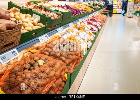 RIGA, LATVIA. 12th March 2026. A wide-angle interior view of a supermarket produce section showing shelves stocked with various potatoes and onions in Stock Photo