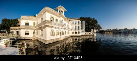This panoramic view shows the white marble Hotel Ahmet Haveli in Udaipur, situated on Lake Pichola with the city skyline visible across the water. Uda Stock Photo