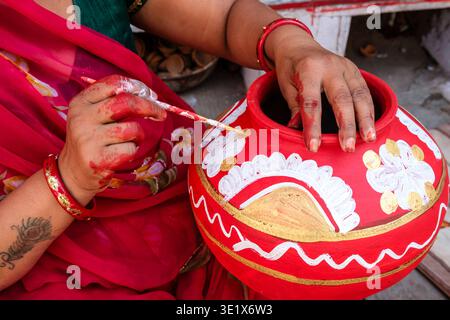 Close-up of a woman in Udaipur decorating a traditional red clay pot with intricate white and gold floral patterns using a small paintbrush. Udaipur R Stock Photo