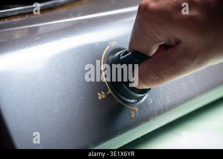 Close up of a human hand rotating a black knob on a grey gas stove to the off position in a domestic kitchen setting. Stock Photo