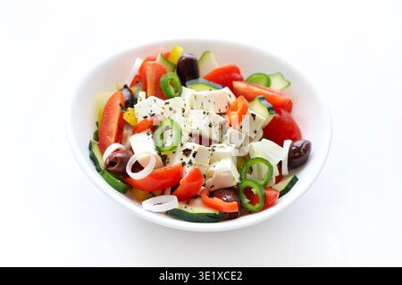 Greek salad with feta cheese and fresh vegetables like tomatoes, pepper, cucumber, onion, olives, origano isolated on white background. Greek cuisine. Stock Photo